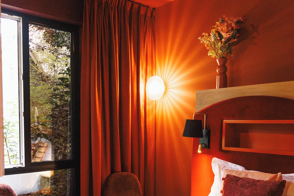 A hotel room with a bed, a chair, a nightstand, and a window with curtains.