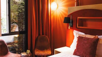 Ein Hotelzimmer mit Bett, Stuhl, Nachttisch und einem Fenster mit Vorhängen.