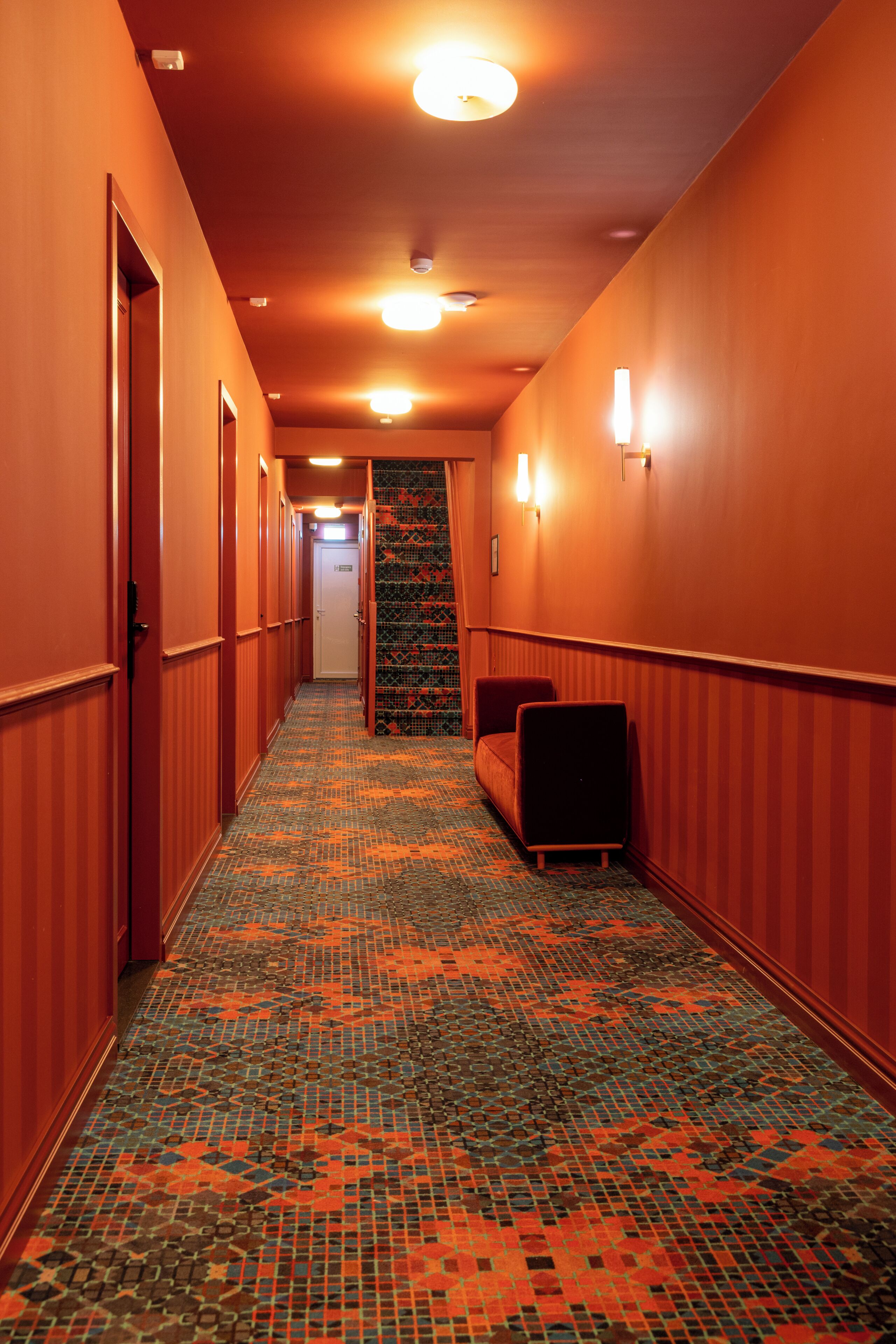 Ein Hotelkorridor mit Teppichmuster, einer Couch und einer Tür am Ende.
