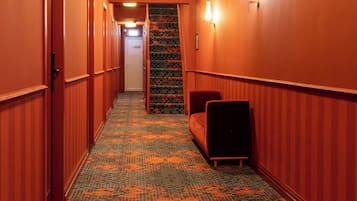 Ein Hotelkorridor mit Teppichmuster, einer Couch und einer Tür am Ende.