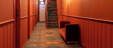 A hotel hallway with a patterned carpet, a sofa, and a door at the end.