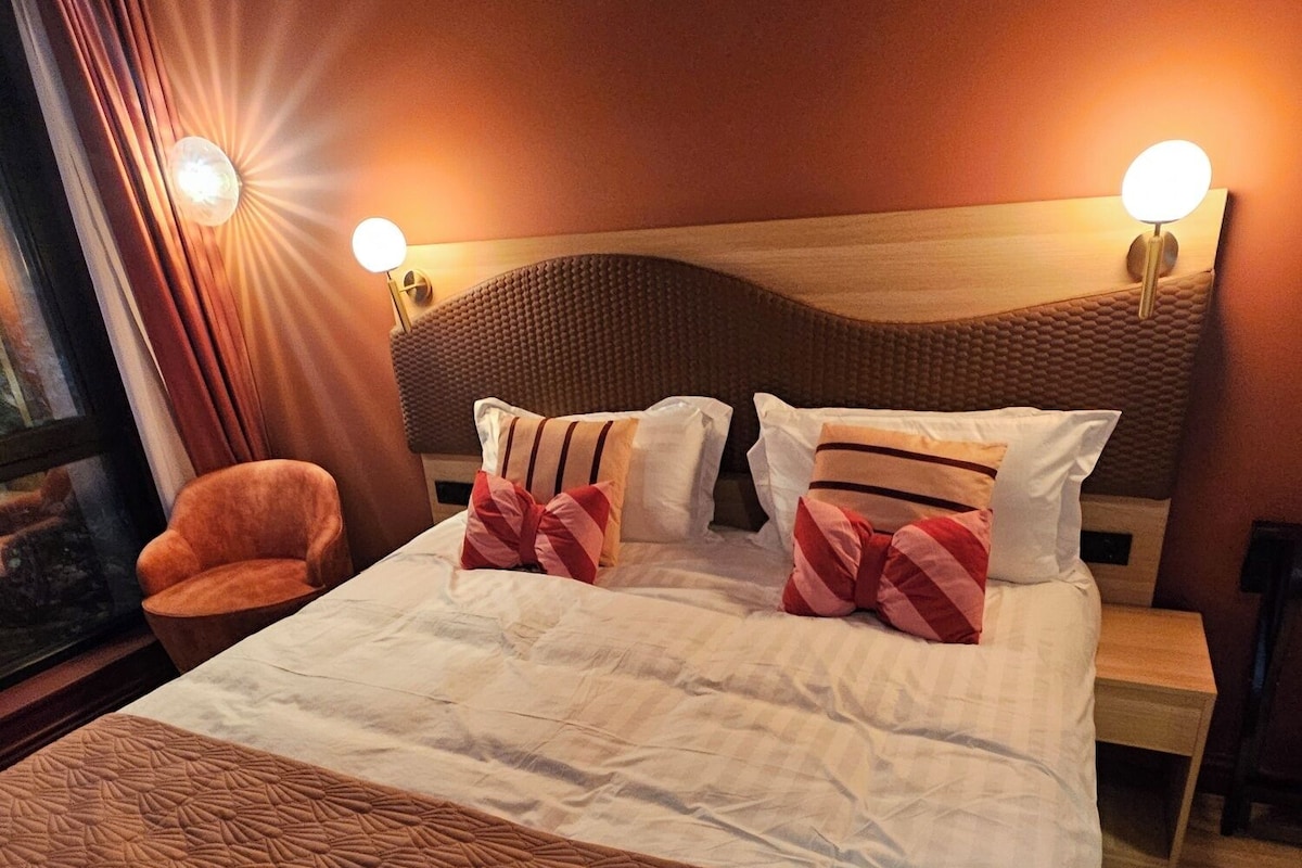 A hotel room with a large bed, two bedside lamps, a chair, and a view of the outside.