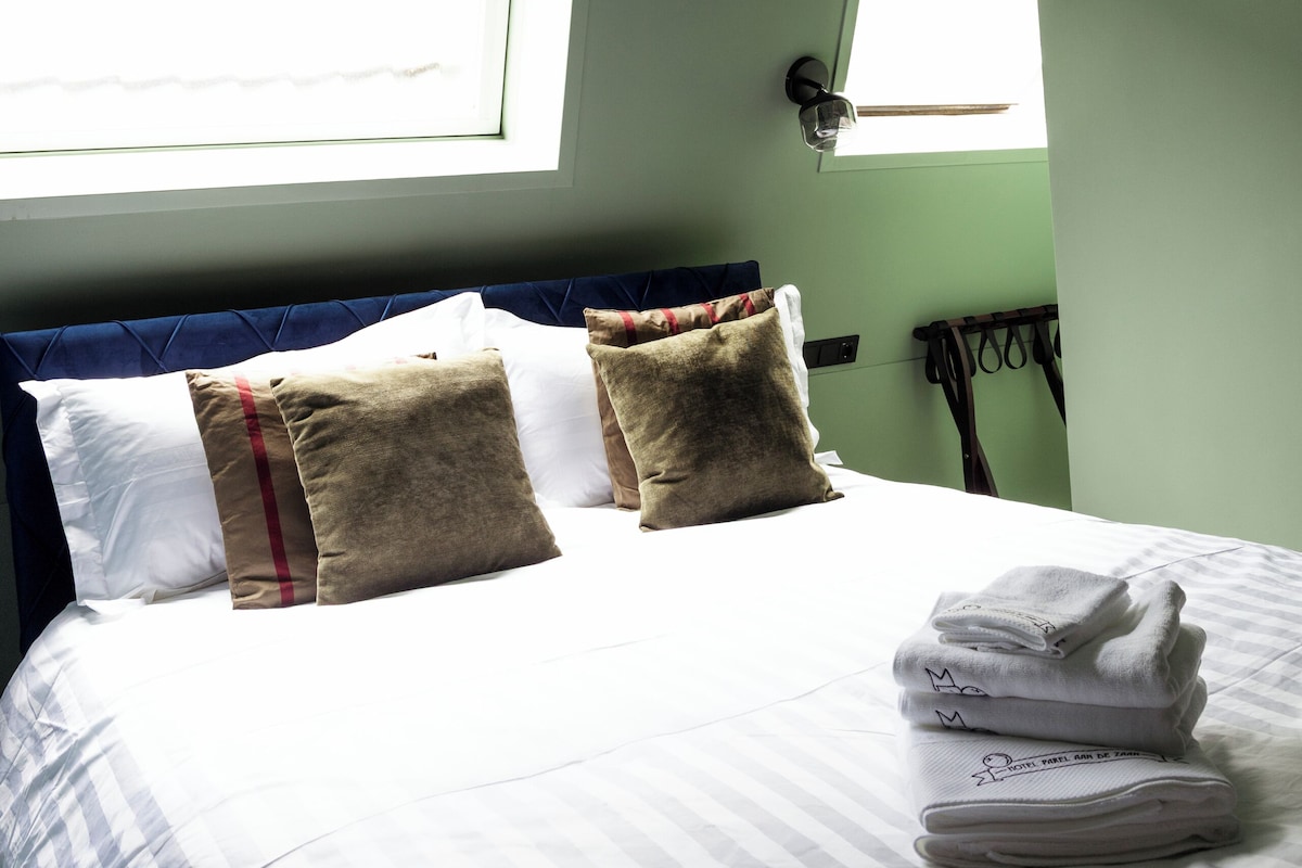 A neatly made bed with white and striped bedding, two pillows, and a stack of folded towels.