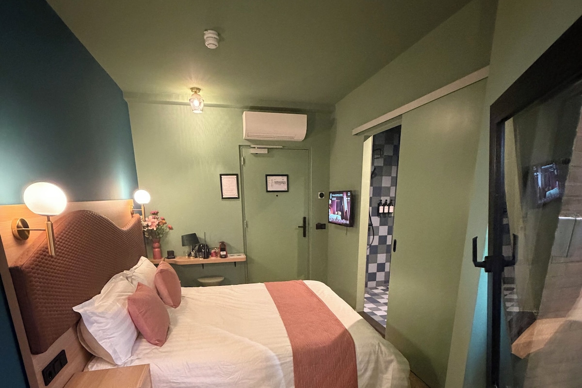 A bedroom with a bed, bedside table, lamp, air conditioning unit, and a television on the wall.