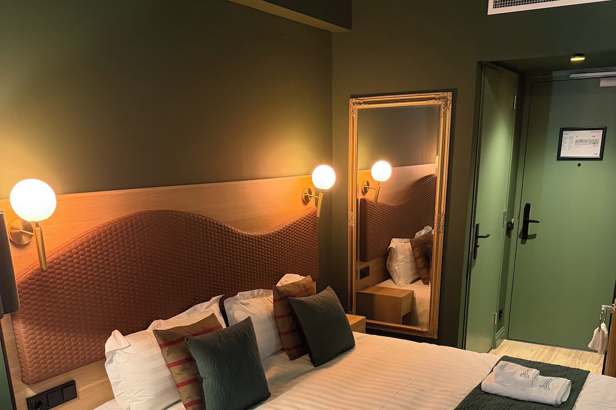 A hotel room with a large bed, bedside tables, a mirror, and a wardrobe.