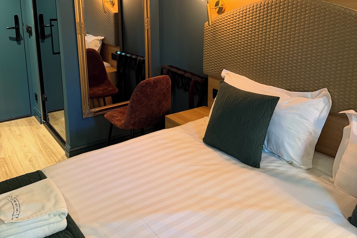A hotel room with a large bed, a chair, a mirror, and a headboard with a textured pattern.