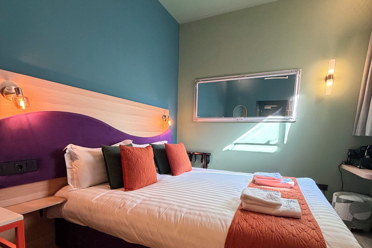 A hotel room with a bed, a desk, a mirror, and a window.
