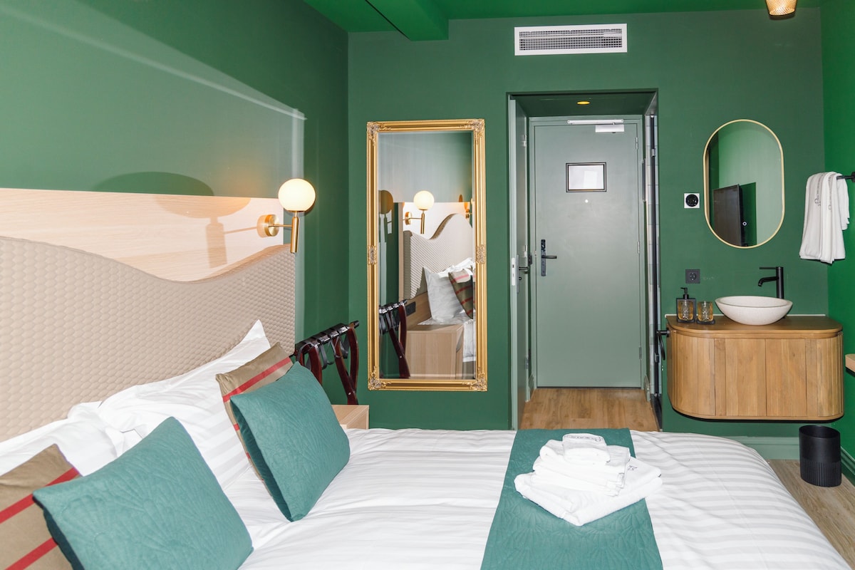 A hotel room with a bed, a bathroom, a mirror, and a sink.