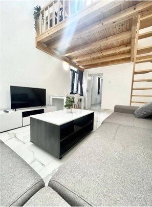 A modern living room with a flat-screen TV, a white console table, a grey sofa, and a wooden ceiling. - Skylit Loft Duplex in Historic Old Town Courtyard (București)