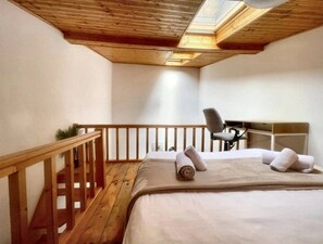 A bedroom with a wooden ceiling, a bed with pillows, a chair, and a small desk. - Skylit Loft Duplex in Historic Old Town Courtyard (București)