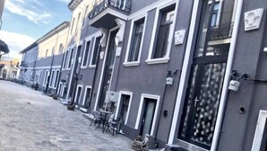 Une rangée de bâtiments bordant une rue pavée, avec des tables et des chaises à l’extérieur, et une croix sur la porte.
