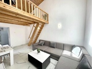 A modern living room with a grey sofa, a white coffee table, and a wooden staircase. - Skylit Loft Duplex in Historic Old Town Courtyard (București)
