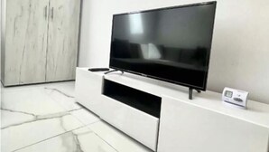 Un salon moderne avec un téléviseur à écran plat posé sur un meuble de rangement blanc, un sol en marbre et une grande armoire.