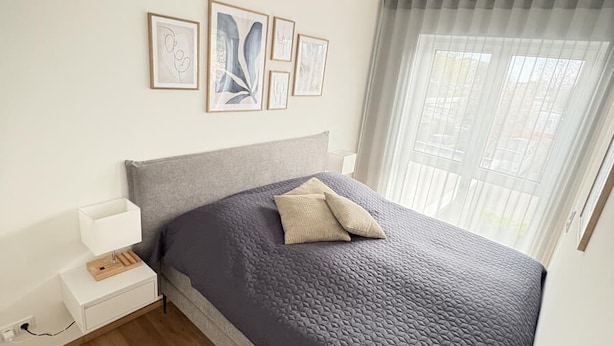 Une chambre à coucher avec un lit, une table de chevet, des œuvres d’art murales et une fenêtre avec des rideaux.