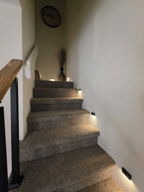 Un escalier avec des marches recouvertes de moquette, une horloge au mur et des lampes fixées au mur.