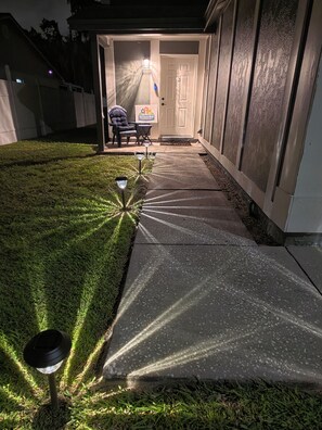 Un chemin menant à l’entrée d’une maison, avec une pelouse et du mobilier d’extérieur.