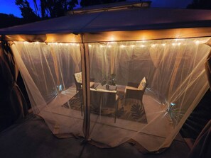 Une tente transparente, avec une table et des chaises à l’intérieur, illuminée par des guirlandes lumineuses.