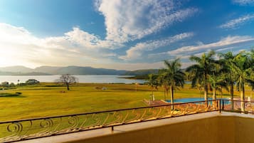 Uma varanda com vista para um campo gramado, um corpo d'água e montanhas ao longe.