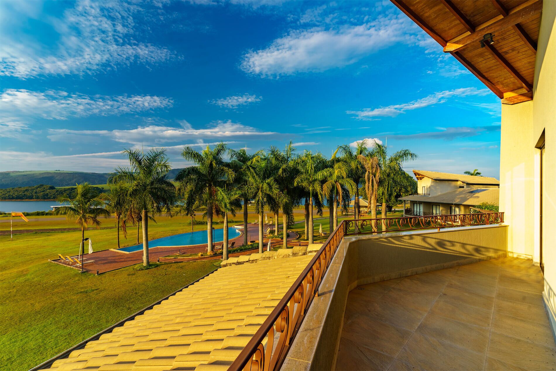 Un balcón con vistas a una piscina, palmeras y una masa de agua distante.