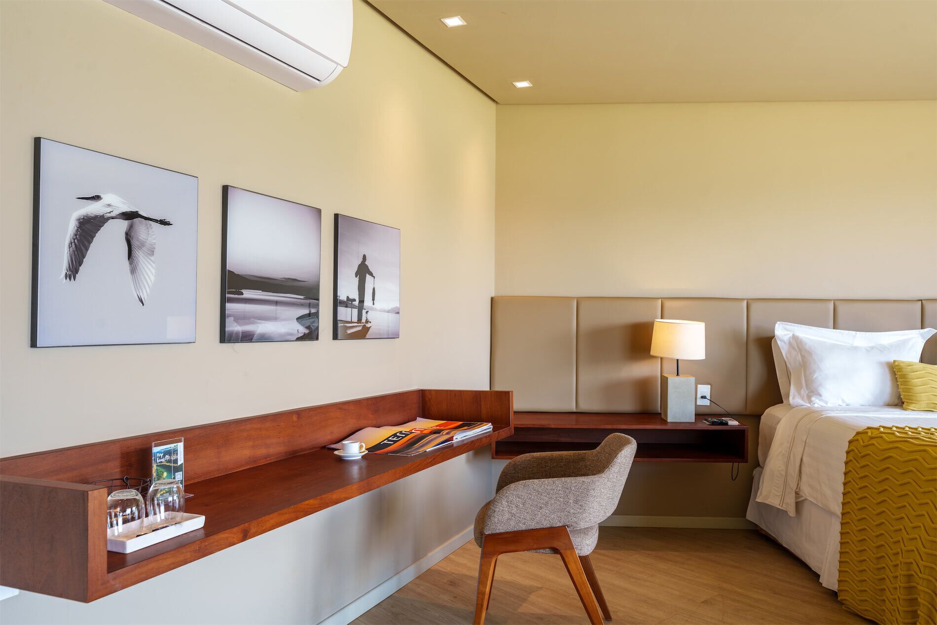 Quarto de hotel com uma cama, uma escrivaninha com cadeira, mesa de cabeceira e decoração nas paredes.