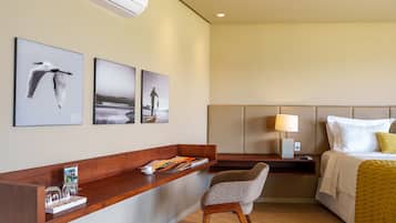 A hotel room with a bed, a desk with a chair, a nightstand, and wall art.