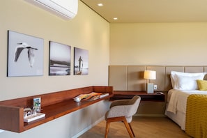A hotel room with a bed, a desk with a chair, a nightstand, and wall art.