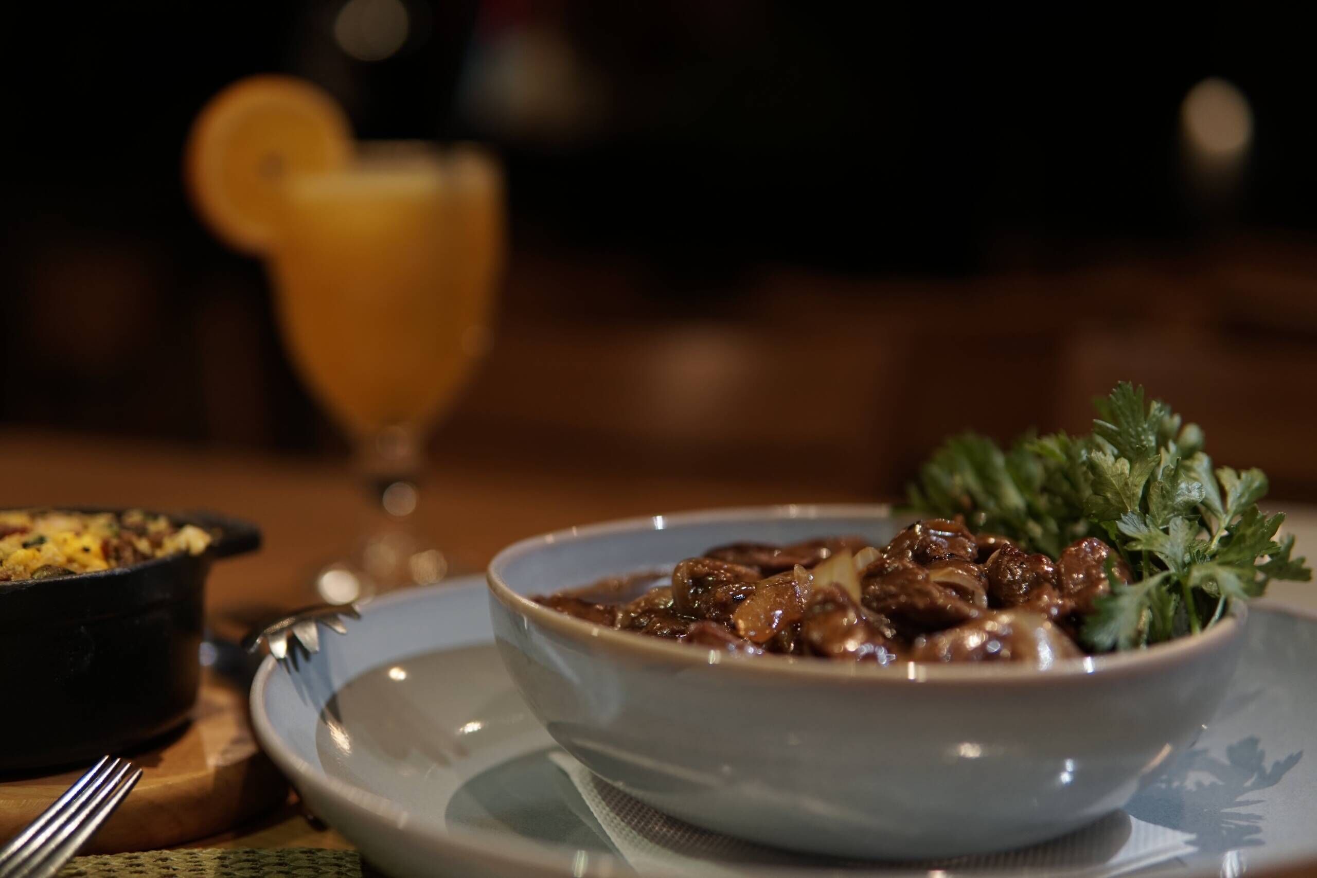 Un bol de chili garni, posé sur une assiette, un verre de jus d’orange et une fourchette sur une table.