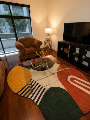 Ein Wohnzimmer mit Sofa, Fernseher, Lampe und einem dekorativen Teppich.