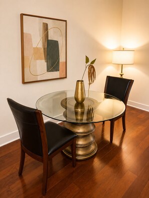 A round glass table with a brass base, two black leather chairs, a vase with a plant, a wall-mounted abstract painting, and a floor lamp. - Uptown Luxe ATL walk to Shops, Dining & MARTA (Atlanta)