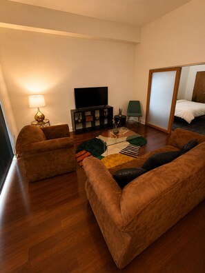 A furnished living room with a sofa set, a television, a lamp, and a mirror. - Uptown Luxe ATL walk to Shops, Dining & MARTA (Atlanta)