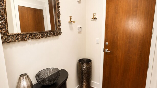 A hallway with a wooden door, a mirror with an ornate frame, a console table with decorative items, and a textured vase. - Uptown Luxe ATL walk to Shops, Dining & MARTA (Atlanta)