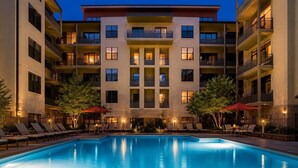 A multi-story hotel with a swimming pool, outdoor seating, and a well-lit facade. - Uptown Luxe ATL walk to Shops, Dining & MARTA (Atlanta)