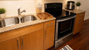 A modern kitchen with wooden cabinets, stainless steel appliances, a double sink, and a striped rug. - Uptown Luxe ATL walk to Shops, Dining & MARTA (Atlanta)