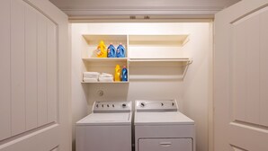 A laundry room with two stacked washers and dryers, shelves with detergent bottles, and hanging towels. - Skyline House with Rooftop views, Cinema, and Game Room in Houston Texas (Houston)