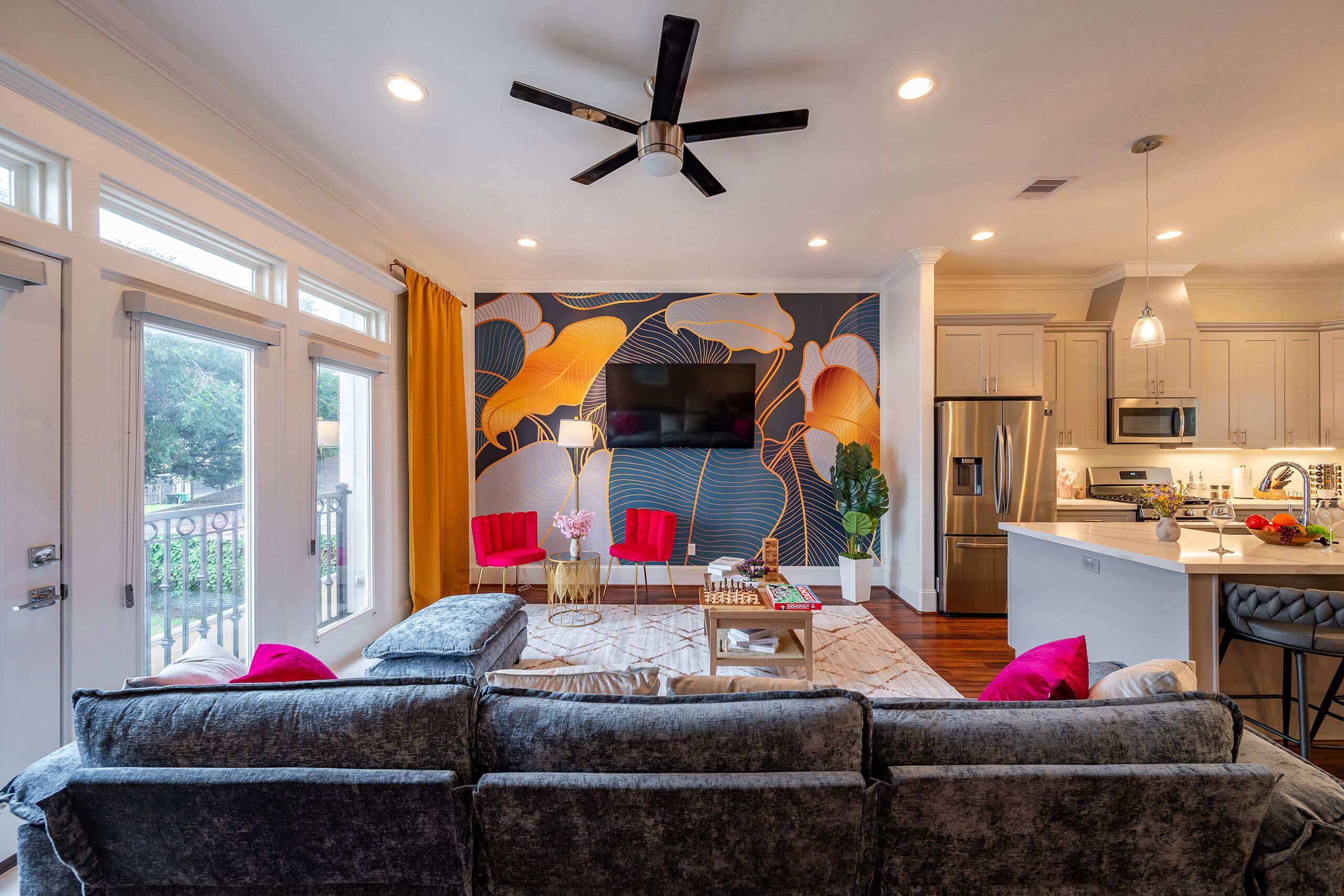 A modern living room with a sofa, a coffee table, and a TV. There is a kitchen area with a refrigerator, microwave, and sink.