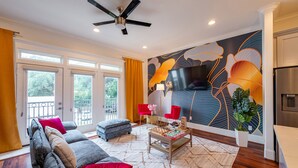 A living room with a sofa, ottoman, coffee table, and a flat-screen TV mounted on the wall. - Skyline House with Rooftop views, Cinema, and Game Room in Houston Texas (Houston)