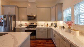A modern kitchen with stainless steel appliances, a central island, and a view of the outdoors through large windows. - Skyline House with Rooftop views, Cinema, and Game Room in Houston Texas (Houston)