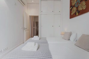 A hotel room with two beds, a hallway leading to a bathroom, and a painting on the wall. - Azul Tile - Super Central, Historical Tiles, AC (Lisboa)