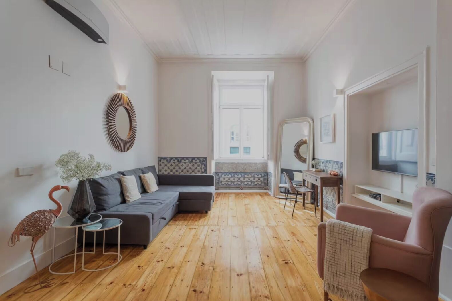A compact living space with a grey sofa, a pink armchair, a wooden floor, and a television on a stand.