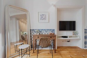 A room with a wooden floor, a dining table with chairs, a TV mounted on the wall, and a tiled backsplash. - Azul Tile - Super Central, Historical Tiles, AC (Lisboa)