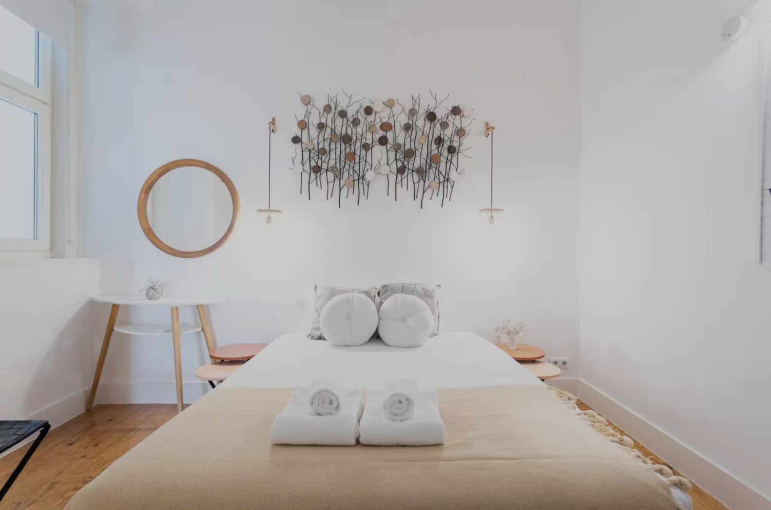 Ein schlichter Schlafzimmerraum mit einem Bett, einem runden Spiegel, einer Wanddekoration und einem kleinen Nachttisch.