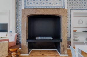 A living room with a fireplace, a television, a pink chair, and patterned wallpaper. - Azul Tile - Super Central, Historical Tiles, AC (Lisboa)