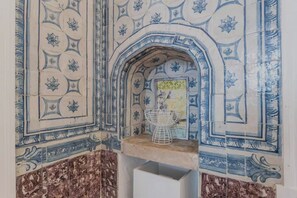 A tiled alcove with a decorative archway, a small table, and a chair. - Azul Tile - Super Central, Historical Tiles, AC (Lisboa)