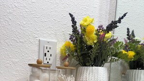 Uma prateleira de madeira com frascos, um vaso com flores e um espelho.