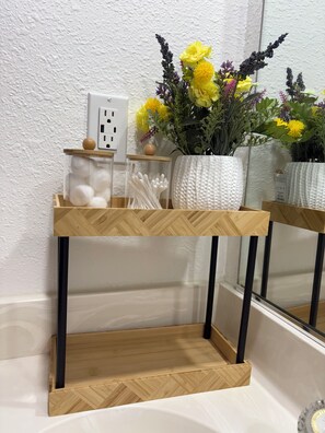 Ein Holzregal mit Gläsern, eine Vase mit Blumen und ein Spiegel.