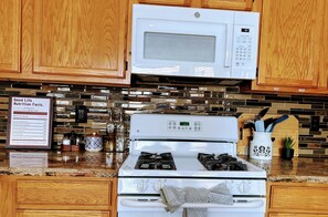 A kitchen with wooden cabinets, a microwave, a stove, and a sign with nutrition facts. - Spacious Home , King Bed, Chef’s Kitchen Near UNR, Downtown & Convention Center (Reno)