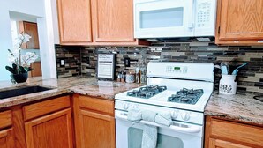 Uma cozinha com armários de madeira, fogão branco, micro-ondas e painel de azulejos.