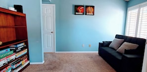 Ein Zimmer mit Bücherregal, Tür, blauer Wand, schwarzem Sofa und zwei Postern mit der Aufschrift 'FOOTBALL' und 'BASEBALL'.