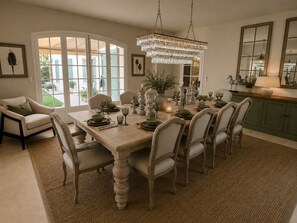 A dining area with a large table set for six, surrounded by chairs, a chandelier, and a view through glass doors. - Luxury Provençal villa recently refurbished to an exceptional standard. (Fayence)
