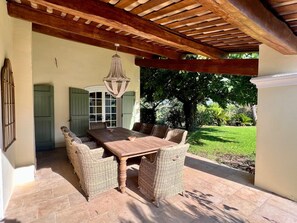 Une terrasse extérieure agrémentée d’une pergola en bois, de meubles en osier et offrant une vue sur un jardin luxuriant.